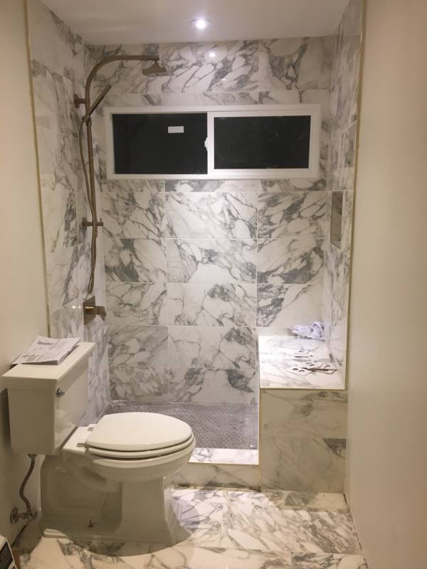 Marble-tiled walk-in shower with rain head and a new toilet